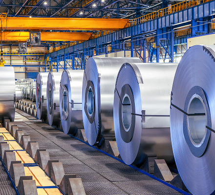Large metal sheet coils lined up inside a modern steel mill.
